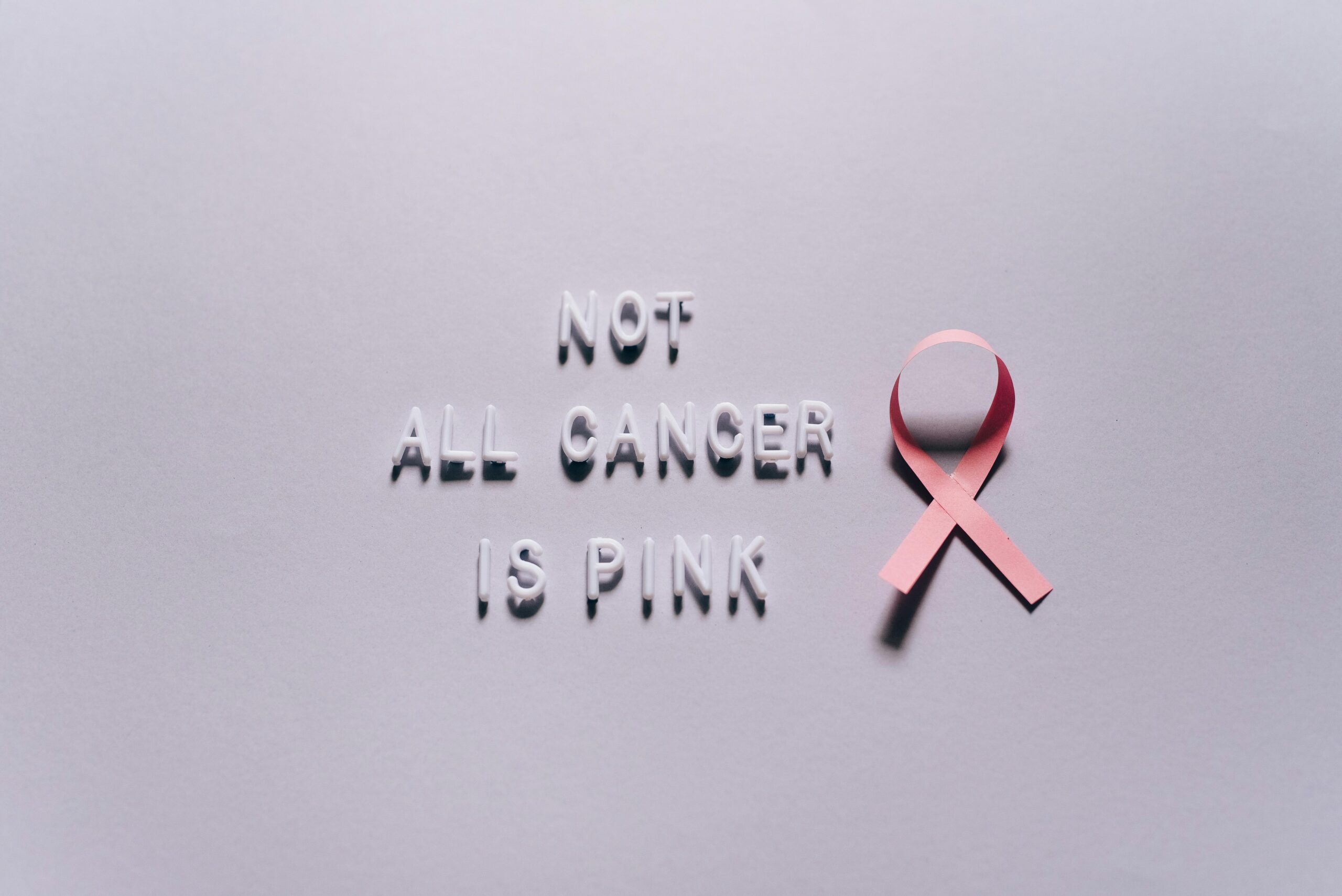 pexels-photo-7857905-7857905 Pink ribbon highlighting diverse cancer awareness on a white surface.